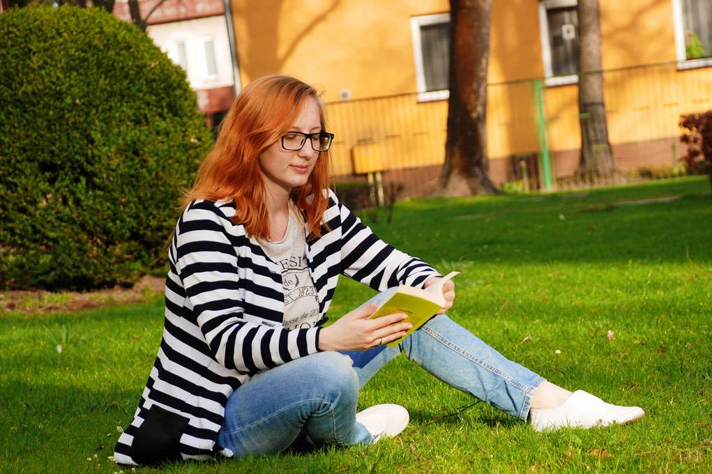 a woman wearing reading glasses reading a book in the grass