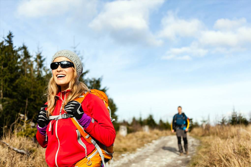 woman in sunglasses and winter clothes on a hiking trail under a blue sky