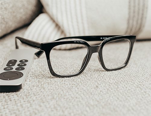 Pair of Visualites designer reading glasses on a couch next to a remote control.